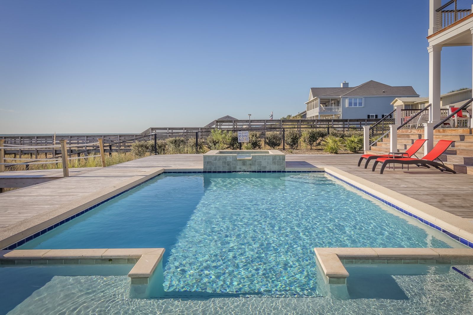 A clean residential backyard pool and spa with clear blue water, deck, and lounge chairs
